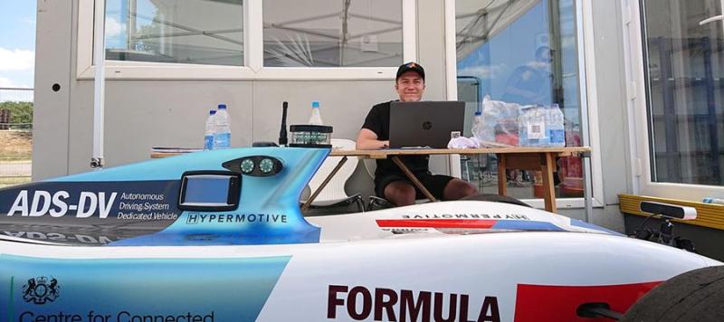 Team member of Formula student with laptop and race car