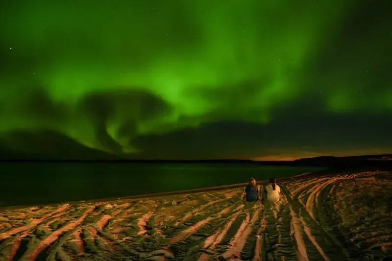 Two women sitting in the beach staring at the Northern lights
