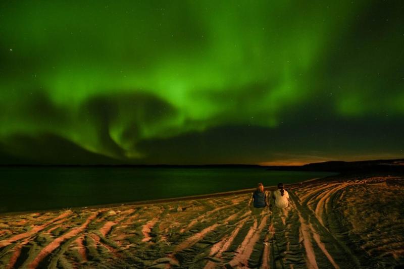 Two women sitting in the beach staring at the Northern lights